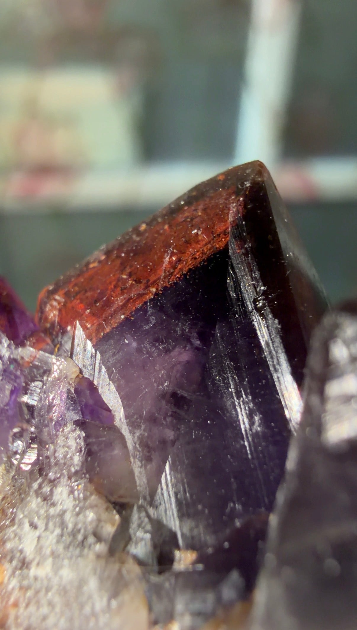 Close-up of a faceted purple crystal point with a prominent reddish-brown top section and surrounding translucent purple material.
