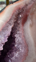 Close-up of a geode crystal cluster with a purple amethyst interior, pink outer layers, and a pale gray outer rim. Item in photo is not the item(s) for sale. 