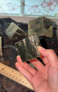 A hand holding a flashy pyrite cube to show its smooth mirror-like surface.