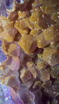 Close-up of a crystalline mineral specimen with golden-brown glittery facets and purple translucent crystal layers visible along the left edge.
