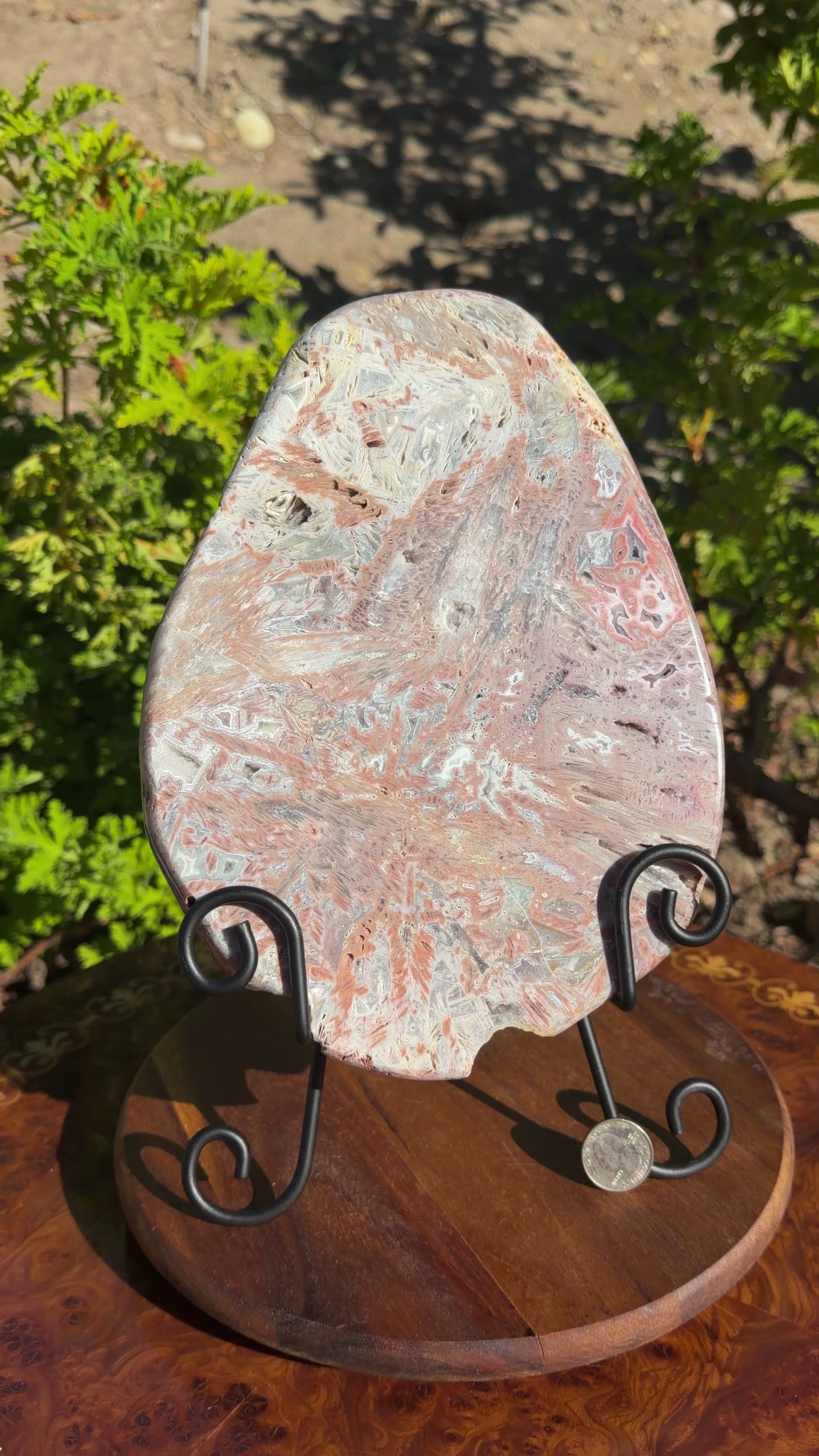 Large egg shaped brazilian pink amethyst plate displayed on a black metal easel. 