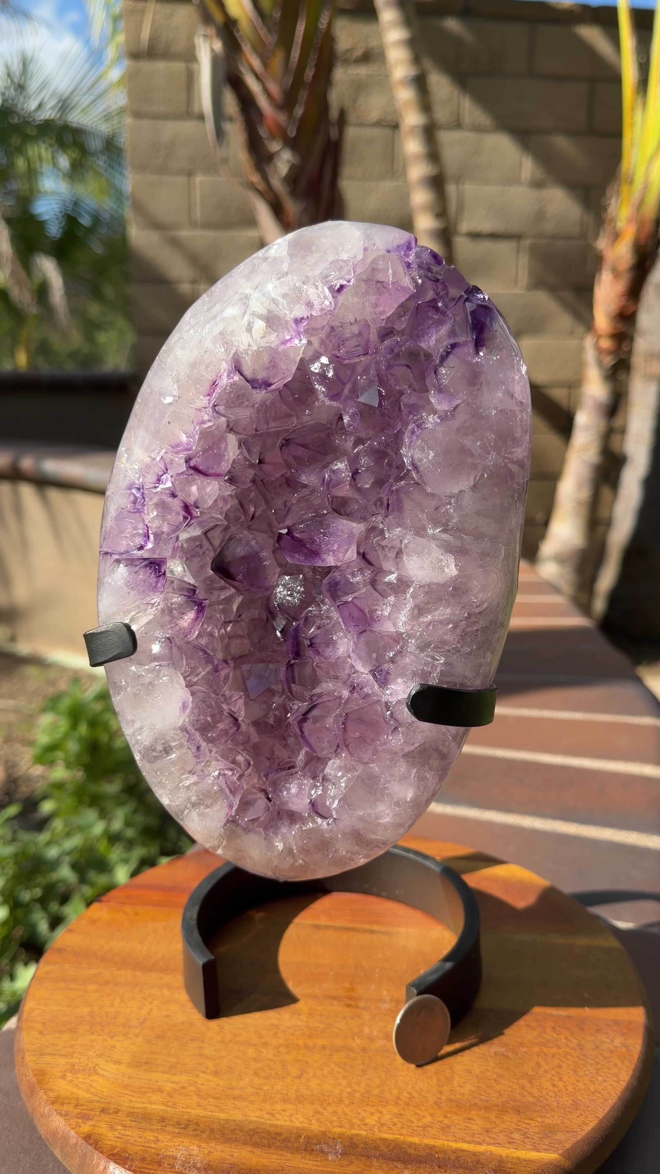 Large oval shaped polished amethyst with a deep purple phantom point cluster face. Held on a black metal stand. Item shown in natural sunlight on a spinning stand.