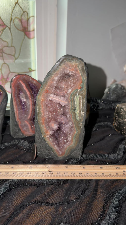Uruguayan purple amethyst with pink/red/green agate banding and a pink toned stalactite bridge slice. Geode is encased in black painted cement to display as a self standing cathedral.