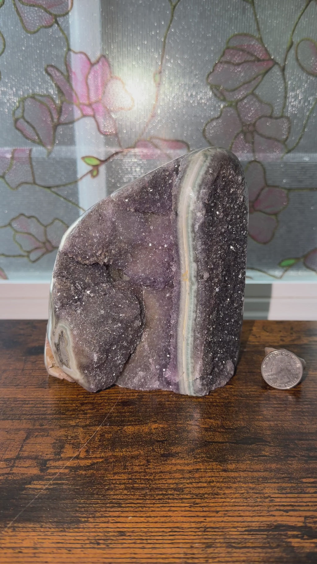 Large Amethyst cut base featuring a large amethyst stalactite slice, druzy orange quartz bridges, and a hidden portal cave. From Brazil. Quarter in view for size reference. Shows cut base in indoor and natural lighting. 

5.5” x 5” x 3.5”