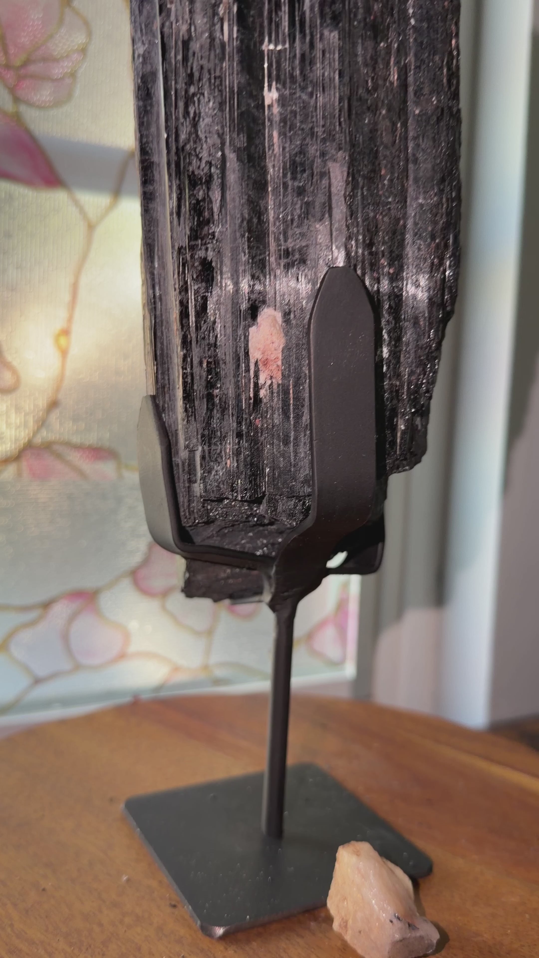 Close up of raw black tourmaline on stand. 
Highlighting the black surface with small bits of gold mica and quartz. Metal black stand included.