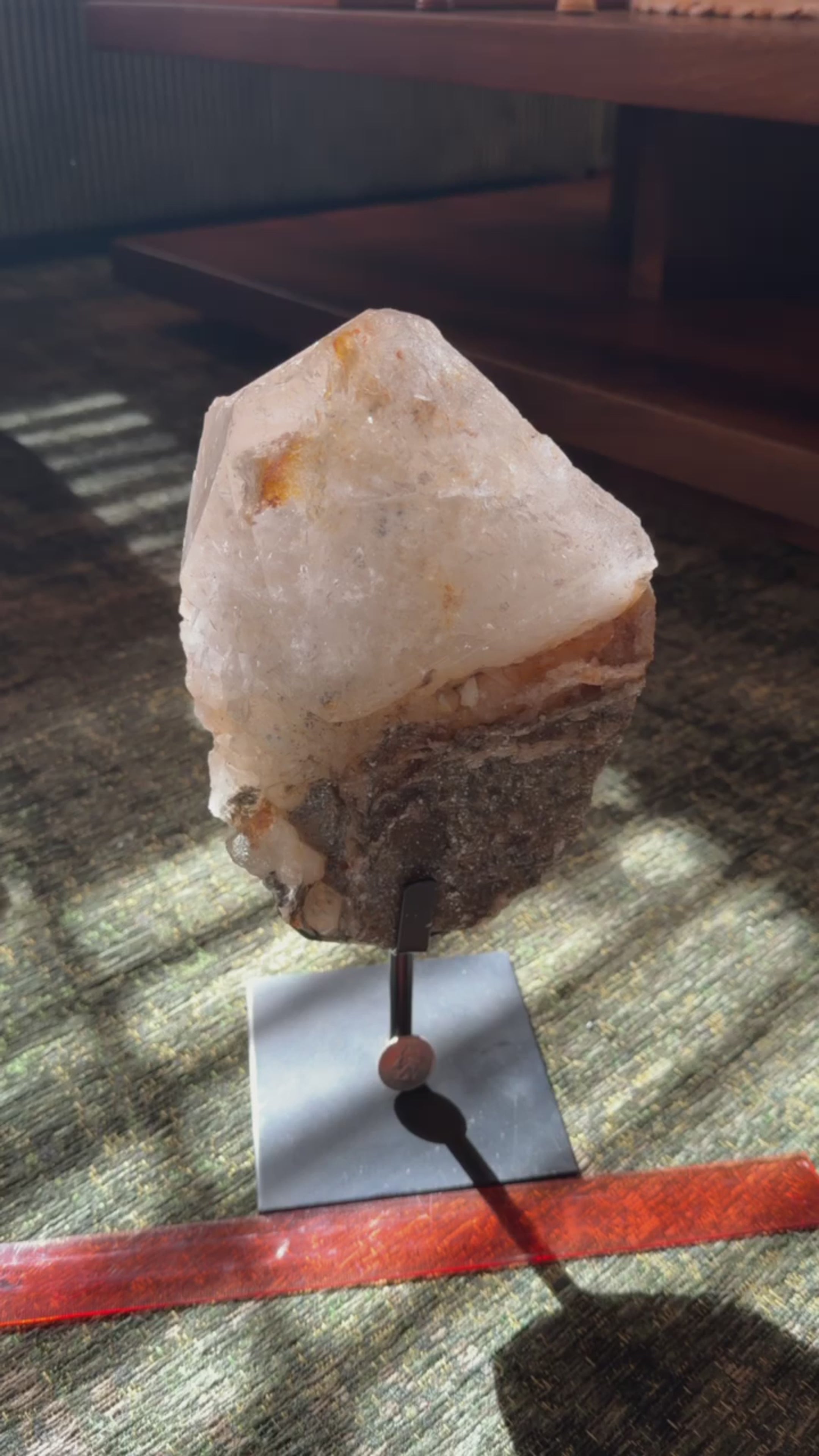Large clear quartz point cluster with warm iron staining and gold mica growths. On fixed black metal stand. 