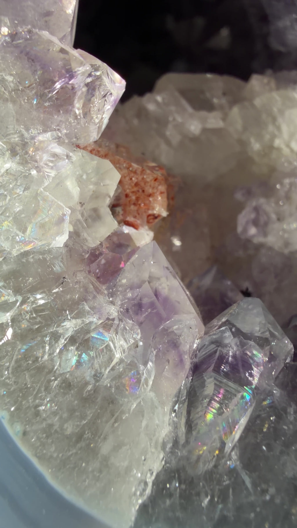 Close up highlighting the rainbows within the amethyst crystals, the blue agate banding, and red hematite inclusions within the calcite.