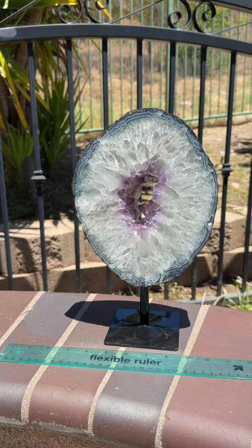 Large Brazilian amethyst portal on spinning stand. Features purple inner core points, rainbow filled white quartz middle layer, and blue agate banding. Sits on a fixed metal black spinning stand. 