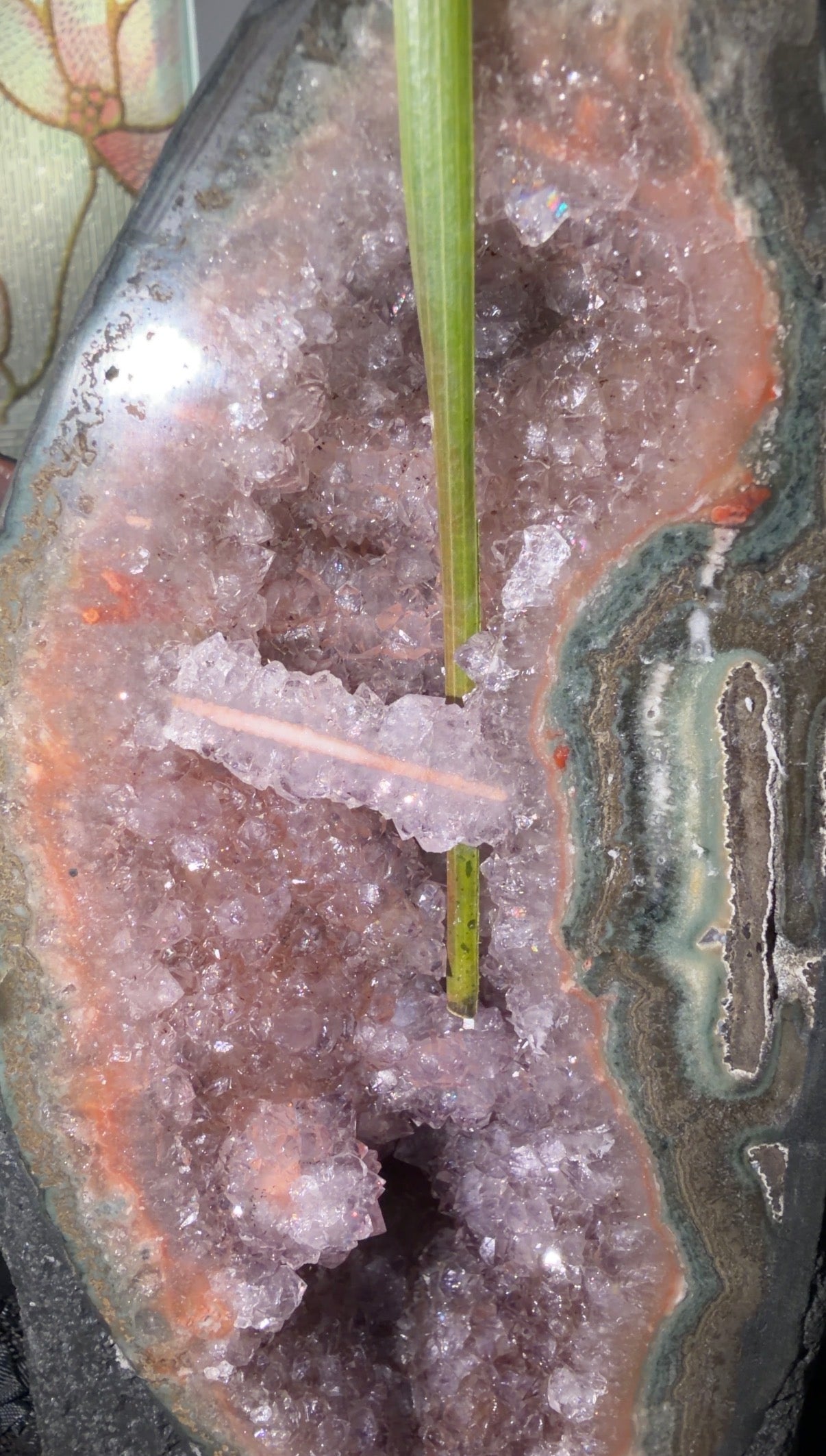 Image shows a leaf going behind the stalactite bridge. Stalactite has a pinky/orange agate core with lilac purple points surrounding. Green and teal agate banding is vibrant on the right side.
